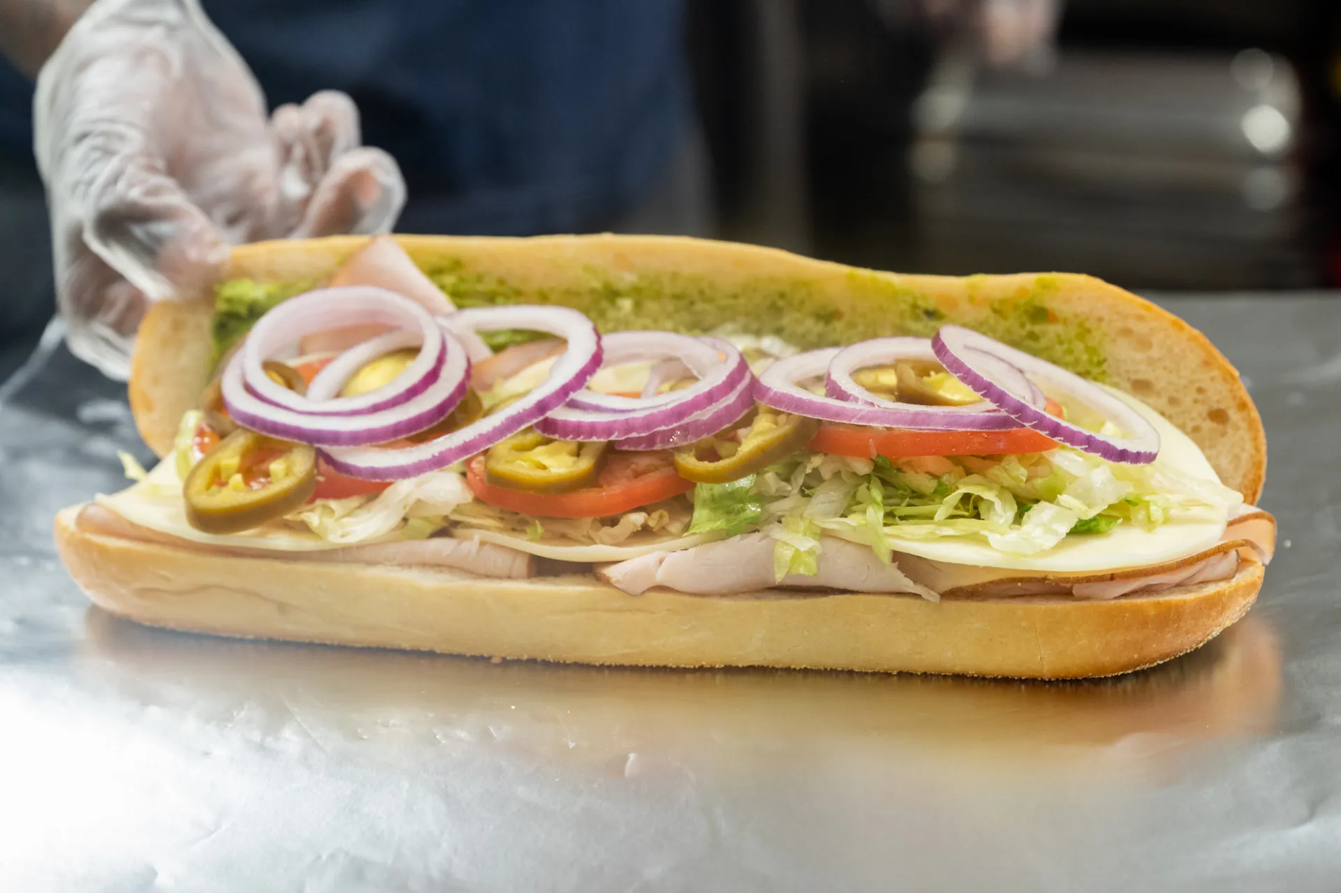 A sandwich with onion, tomato, jalapeno, lettuce, cheese, and deli meat